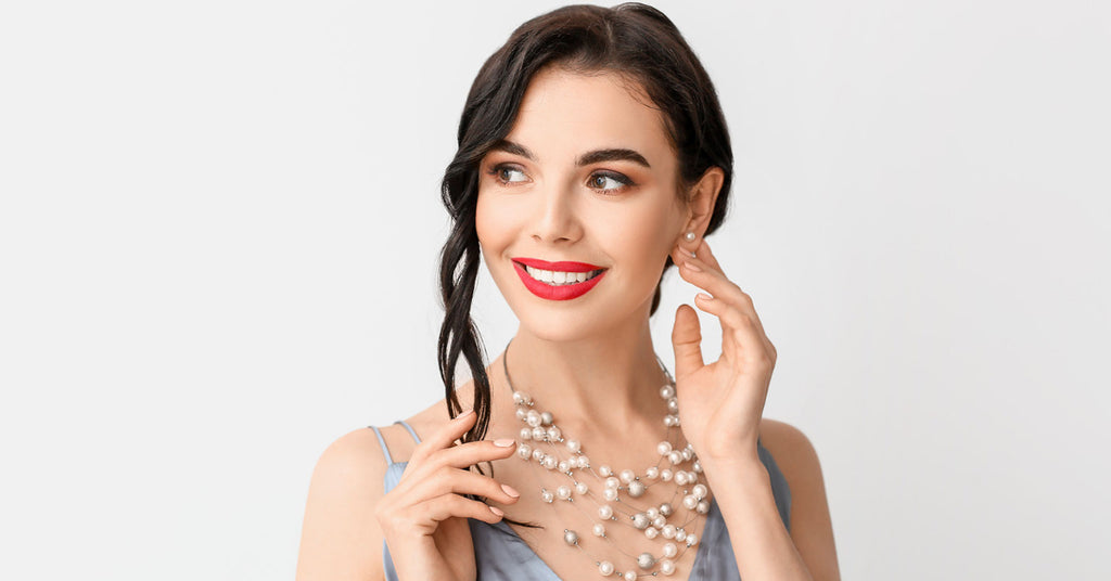 A woman wearing a pair of pearl earrings and necklace. She's smiling.Protect your jewelry by following these 5 tips.