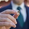 A groom holds a men's wedding band in front of him as one half the bridal rings for the ceremony. 