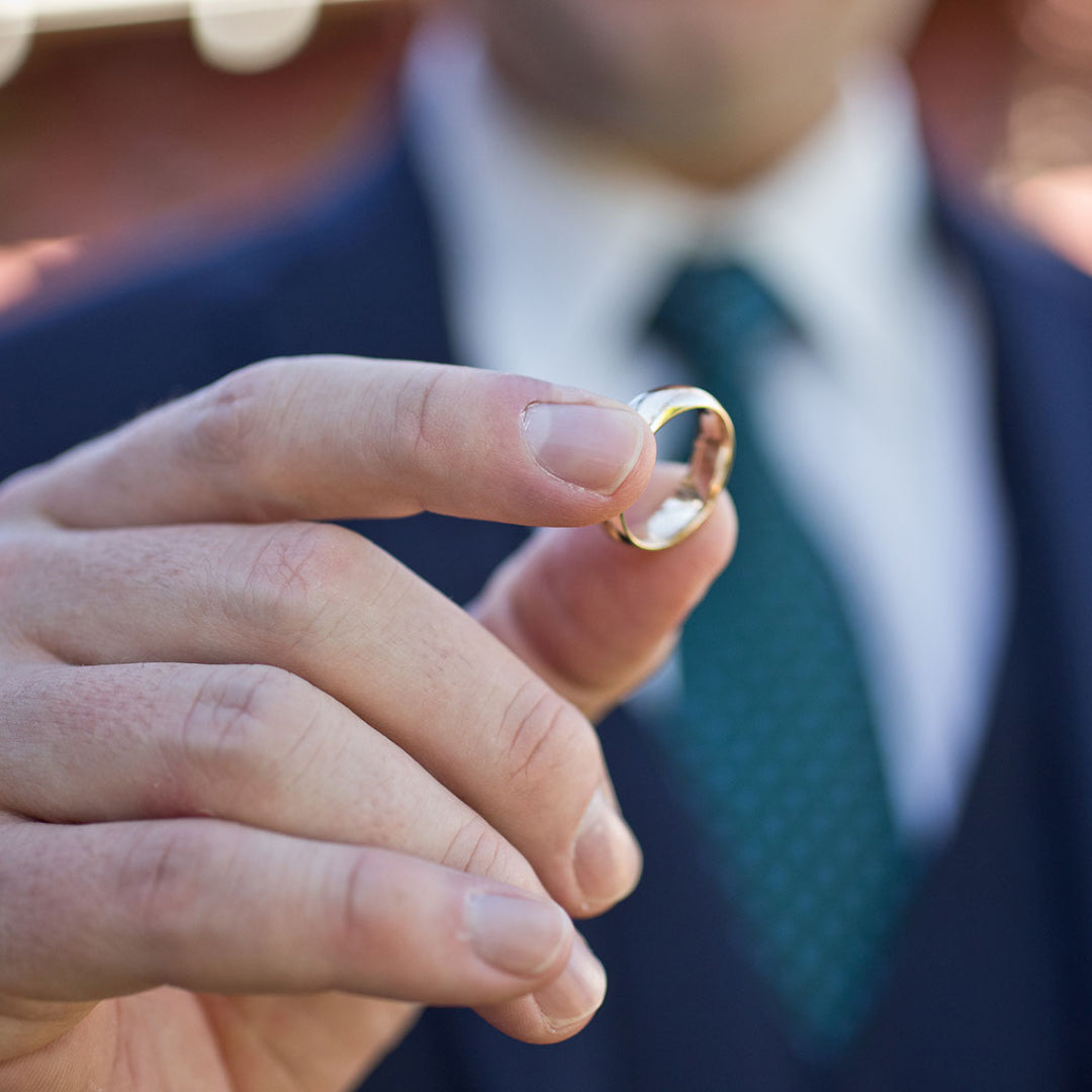 A groom holds a men's wedding band in front of him as one half the bridal rings for the ceremony. 