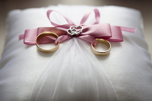 Men's wedding bands and women's wedding bands on a satin pillow tied together with a pink bow.