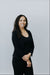 Woman in a black outfit standing against a plain background