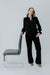 Woman in a black outfit standing next to a gray chair on a white background